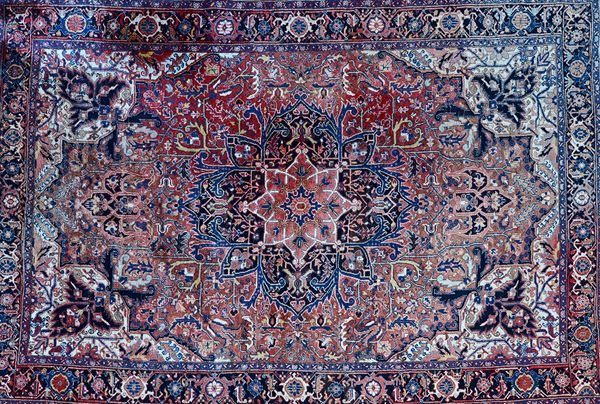 A Heriz carpet, Persian, the madder field with a bold shaped medallion, ivory spandrels, all with angular floral sprays, an indigo palmette and vine b