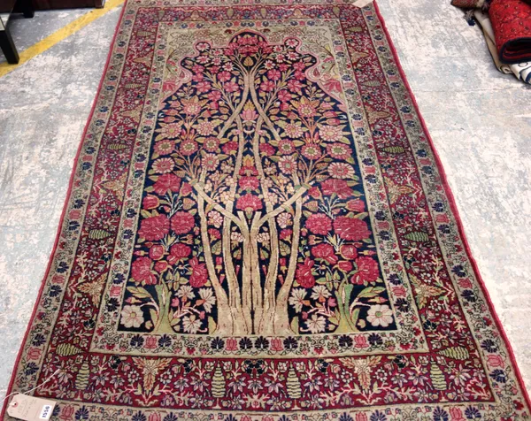 A Kerman Laver Tree of Life prayer rug, Persian, the dark indigo mehrab with an abundantly floral tree, rising to an ivory floral arch, a madder flora