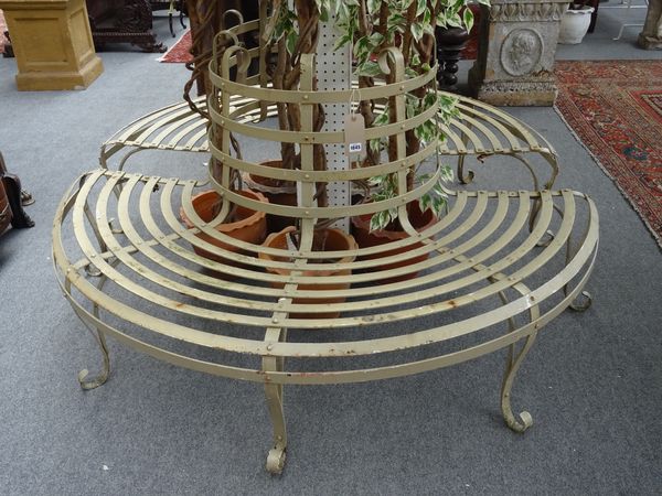 A Regency style cream painted wrought iron tree guard bench, circa 1900, with slatted seat and scroll supports, 175cm diameter x 87cm high.