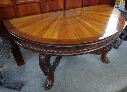 A 19th century Anglo-Indian console table, the specimen wood radial veneered semi-elliptic top on a pair of floral carved lion's paw supports, united