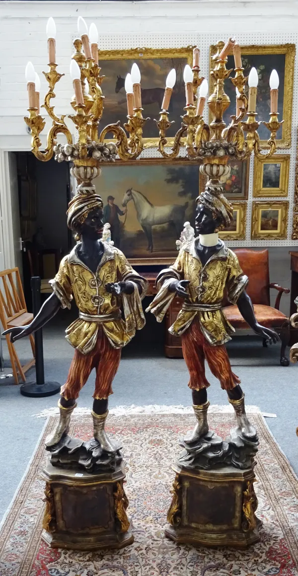 A pair of resin Blackamoor candelabra, each polychrome painted figure mounted with a nine branch candelabrum, on a parcel gilt lozenge shaped base, 21