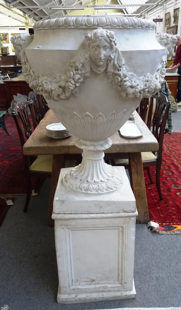 A large pair of white resin Neo-Classical Revival urns, each with floral swag and face mask decoration, on fluted socle and square base, 85cm wide x 1