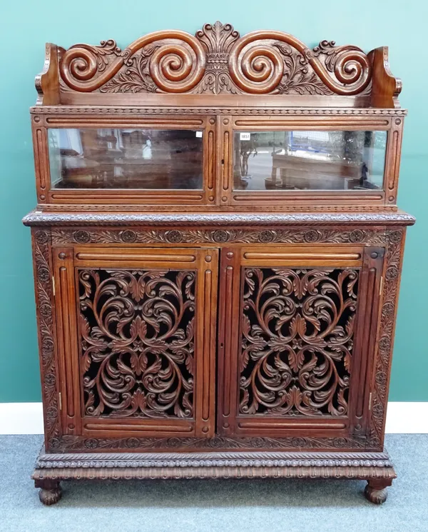 A mid-19th century Anglo-Indian teak side cabinet, the scroll carved back over pair of glazed doors, the base with pair of open carved foliate doors,