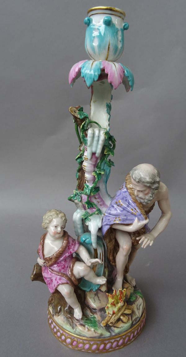 A Meissen  porcelain figural candlestick, 19th century, emblematic of Winter, modelled with an old man wearing a fur lined cloak with attendant putto