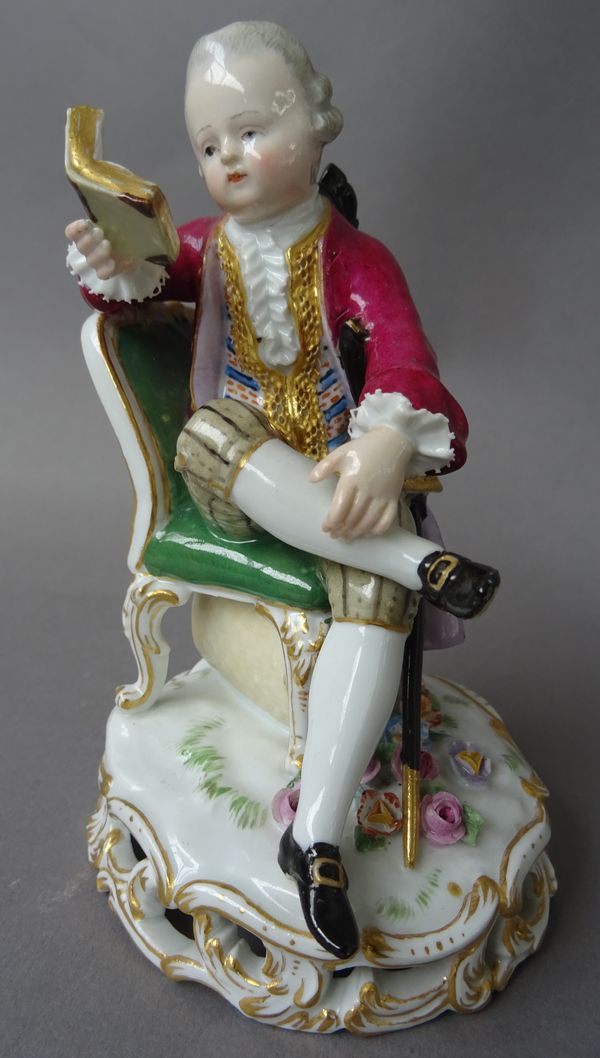 A Meissen porcelain figure of a boy reading a book, circa 1900, incised C28, stamped 127, blue crossed swords mark, the seated child over a gilt scrol