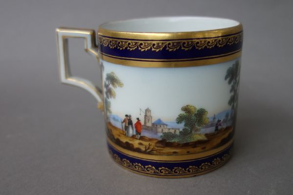 A Berlin porcelain cabinet cup, 19th century, hand painted with a banded landscape within a gilt foliate cobalt blue border, printed marks. (6cm high)