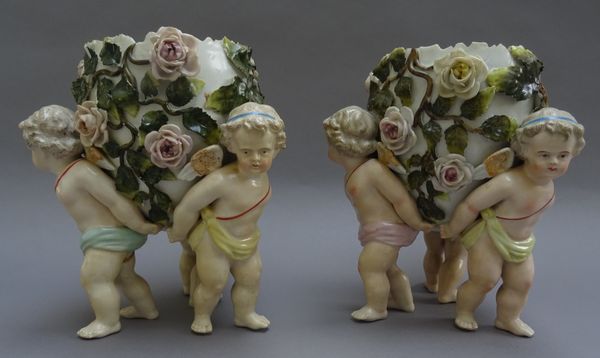 A pair of Sitzendorf porcelain figural jardinières, early 20th century, each 'egg' form bowl encrusted with flowers, held aloft by three putti,  blue