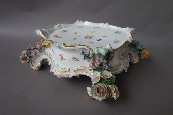 A Meissen porcelain stand, late 19th century, of shaped square form, painted with flowers and insects, the scroll moulded supports applied with flower