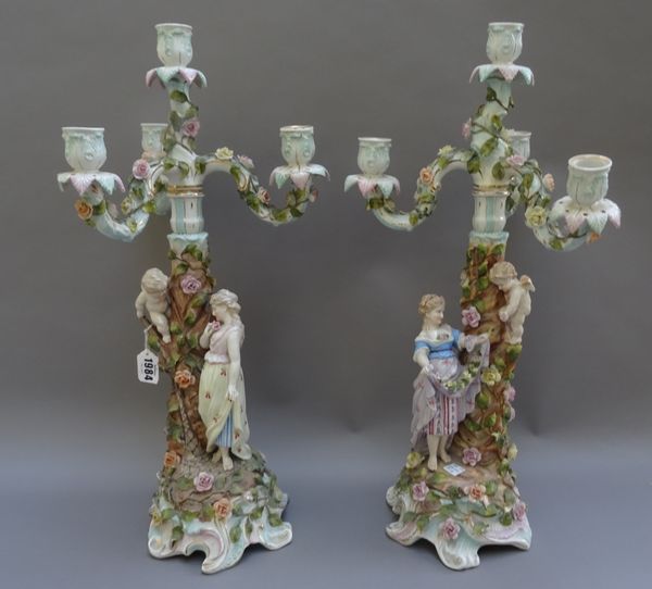 A pair of Sitzendorf four-light candelabra, late 19th century, each modelled with a young woman and a putto around a tree, beneath three scroll arm br