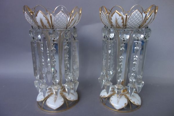 A pair of glass table lustres, late 19th century, each overlaid in white with petal shaped panels picked out in gilding and hung with prism drops, 27.