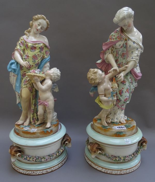 A large pair of German porcelain figure groups with matching bases, late 19th century, each modelled as a classical young woman standing with a putto,