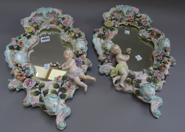 A pair of Sitzendorf wall mirrors, late 19th century, of rococo form, each applied with a putto and encrusted with flowers and fitted with three scrol