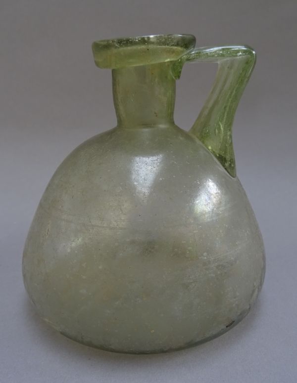 A Roman pale green glass flask, circa 3rd-4th century A.D, of compressed form set with wide strap handle, 13.5cm. high.Provenance: Christie's London,