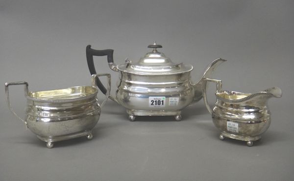 A silver three piece tea set, comprising; a teapot, a twin handled sugar bowl and a milk jug, each piece having a decorated rim and raised on four sph