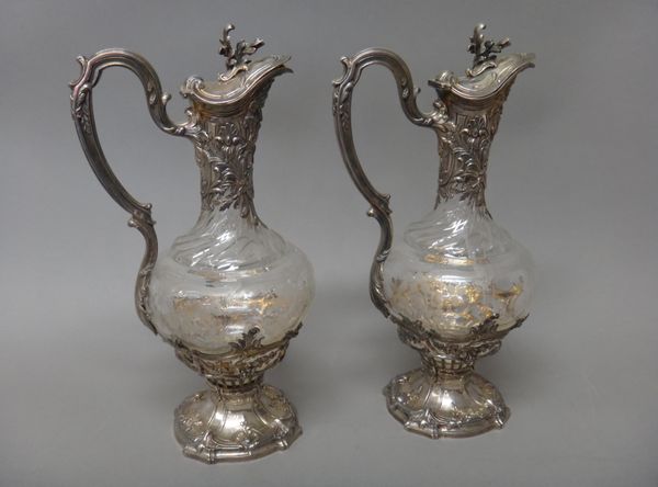 A pair of French claret jugs, with acid etched glass bodies with floral and foliate decoration below swirled fluting, the mounts with masks to the spo