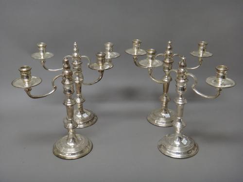 A set of four silver two light table candelabra, each with scrolling arms and raised on a circular base, (loaded), height 32cm, London 1989, retailed