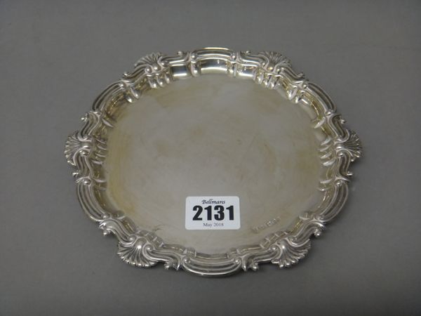 A silver shaped circular card tray, decorated with a scrolled border, raised on three bun feet, diameter 17.5cm, Sheffield 1900, weight 172 gms.