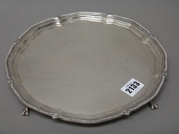 A silver salver, of shaped circular form, decorated with a beaded rim, raised on four ball and claw feet, diameter 25.5cm, Sheffield 1923, weight 495