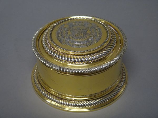 A silver gilt box and cover, of circular form, decorated with gadrooned rims, the detachable cover monogram engraved to the centre, within a Rococo ca