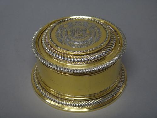 A silver gilt box and cover, of circular form, decorated with gadrooned rims, the detachable cover monogram engraved to the centre, within a Rococo ca