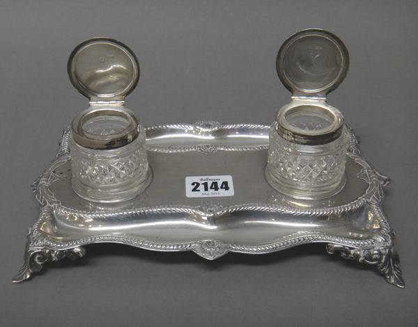 A silver shaped rectangular twin bottle inkstand, decorated with gadrooned rims, raised on four foliate feet, length 24cm, London 1900, with two assoc