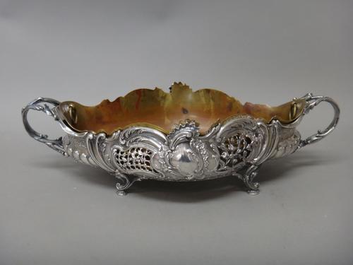 A French twin handled table centrepiece bowl, of shaped oval form, with scroll and floral embossed and pierced decoration, raised on four scroll pierc