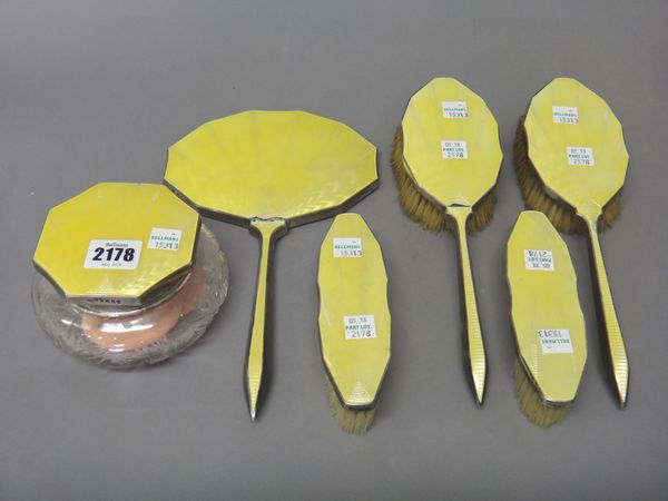 A lady's silver and yellow enamel mounted six piece part dressing set, comprising; a faceted glass lidded powder bowl, a hand mirror, a pair of hair b