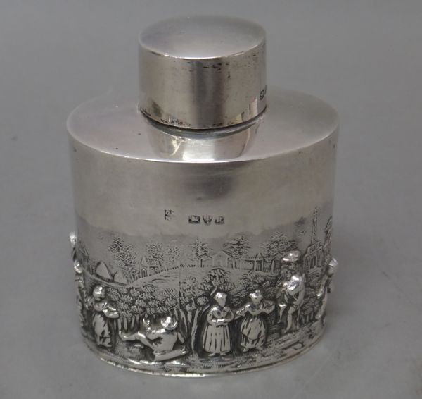 A silver tea caddy, of oval form, with a pull-off lid, the body embossed with various Dutch style figures, in a wooded landscape, with distant buildin