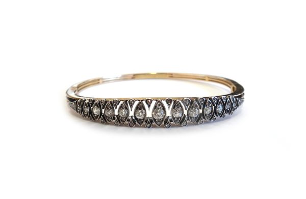 A gold and silver fronted, diamond set oval hinged bangle, mounted with a row of cushion shaped diamonds, in lozenge shaped settings, graduating in si