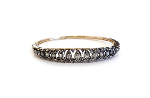 A gold and silver fronted, diamond set oval hinged bangle, mounted with a row of cushion shaped diamonds, in lozenge shaped settings, graduating in si