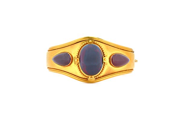 A Victorian gold and carbuncle garnet set oval hinged bangle, circa 1860, mounted with the principle oval carbuncle garnet, within a beaded surround t