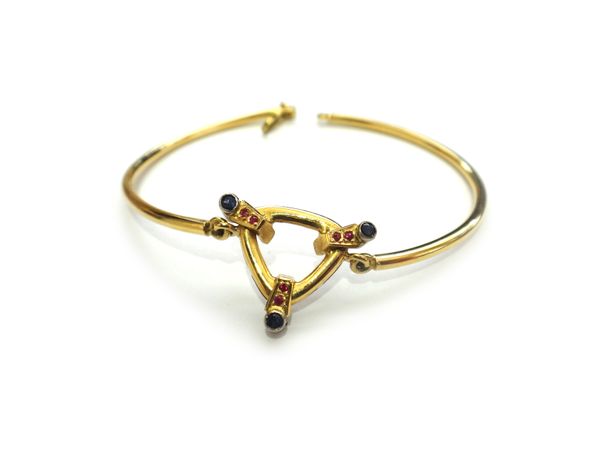 A gold, sapphire and red gem set bracelet, formed as two semi-circular bars, with an openwork gemstone set trefoil shaped motif at the centre, with a