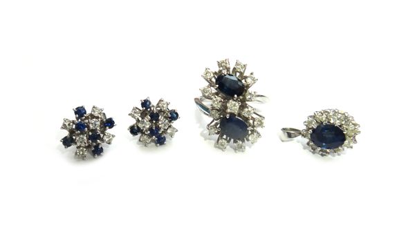 A sapphire and diamond ring, in a twin cluster crossover design, claw set with two oval cut sapphires, within surrounds of circular cut diamonds, ring