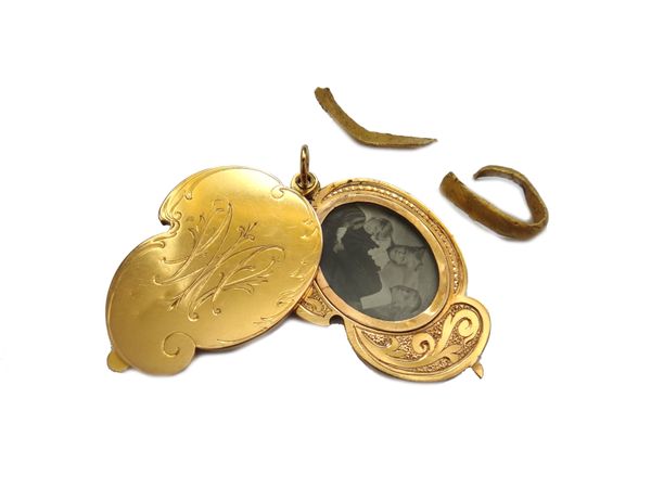 A gold shaped oval hinged pendant locket, opening to reveal two photographic locket compartments, otherwise with engraved decoration and two sections