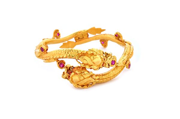 An Indian gold and red gem set hinged bangle designed as two undulating intertwined dragons.   Illustrated