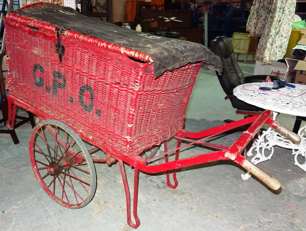 An early/mid-20th century G.P.O portable mail basket, the red wicker work basket with canvas cover, on a wood and steel frame, with wirework wheels an
