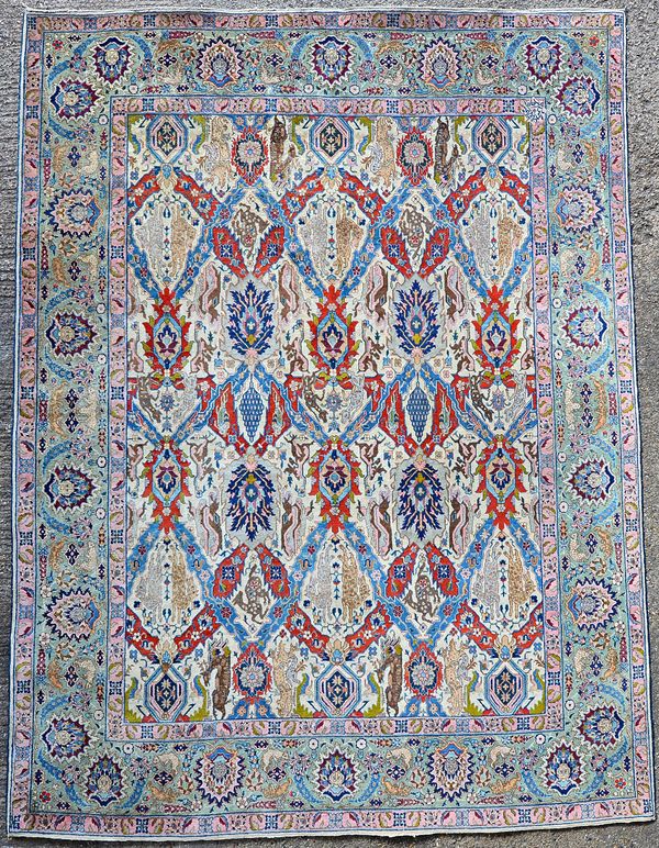 A Tabriz trellis carpet, Persian, the ivory field with a madder and indigo trellis, each section bearing an animal or grapes, four large palmettes, a