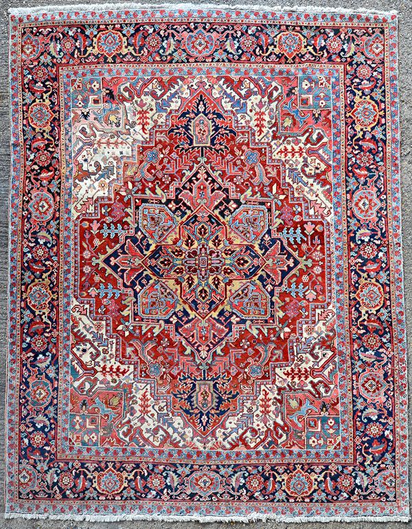 A Heriz carpet, Persian, the ivory field with a madder diamond bearing a bold dark indigo/black pole medallion, minor spandrels; a dark indigo/black b