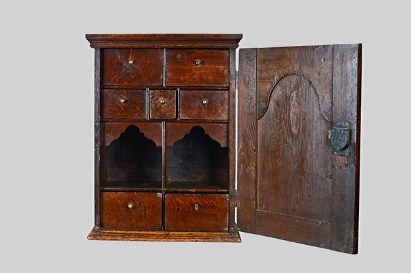A 17th century oak spice cupboard, the arch panel door enclosing a seven drawer and twin recess interior, 47cm wide x 62cm high x 25cm deep. Illustrat