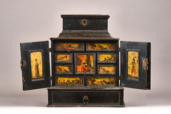 A 17th century North European ebonised table cabinet, the hinged lid over a pair of doors enclosing nine drawers painted with landscape scenes over on
