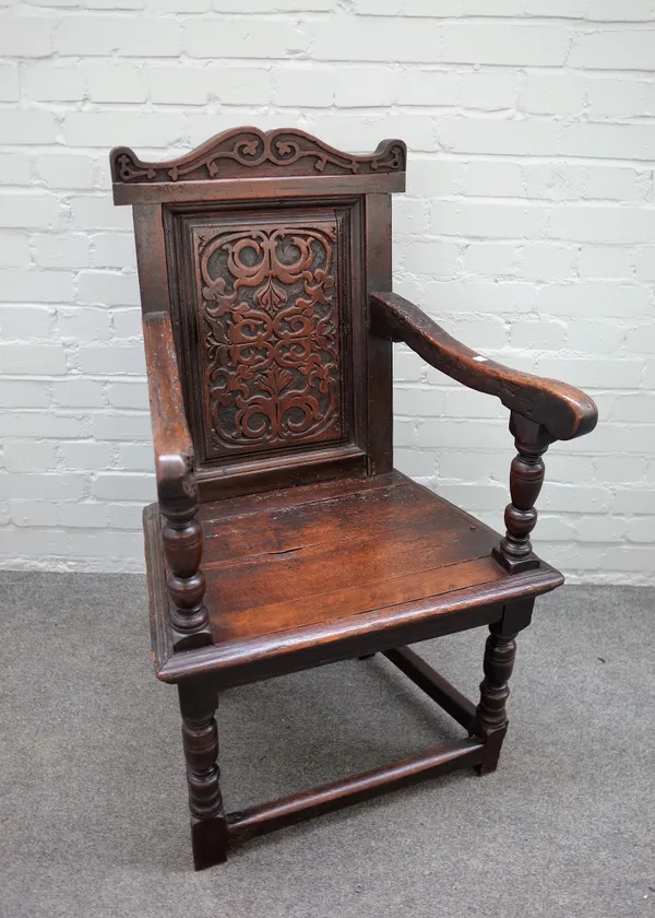 A 17th century walnut Wainscot open armchair with carved panel back on turned supports, united by perimeter stretcher, 62cm wide x 105cm high.
