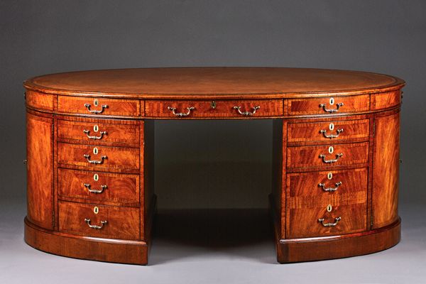An 18th century style crossbanded walnut oval pedestal desk with ten drawers about the knee and dummy opposing, each short end with a pair of cupboard