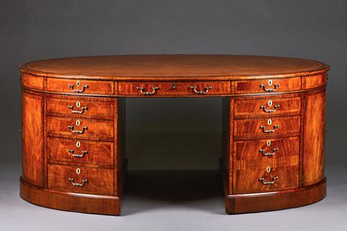An 18th century style crossbanded walnut oval pedestal desk with ten drawers about the knee and dummy opposing, each short end with a pair of cupboard