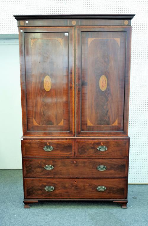 A George III inlaid mahogany linen press with a pair of panelled doors enclosing linen trays over two short and two long drawers on square ogee bracke