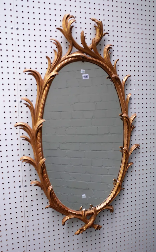 A George III gilt framed mirror, the oval plate within a gadrooned and foliate scroll frame, 66cm wide x 110cm high.
