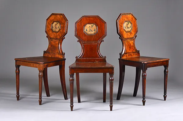 A set of three late George III mahogany hall chairs, each with octagonal back, polychrome painted with heraldic crest over solid seat on turned suppor