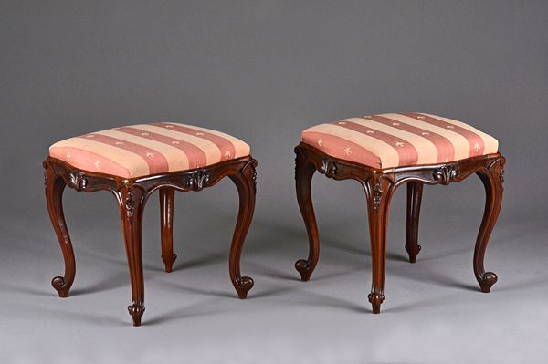 A pair of Victorian rosewood framed footstools of square serpentine outline on floral carved cabriole supports, 50cm wide x 46cm high. Illustrated.