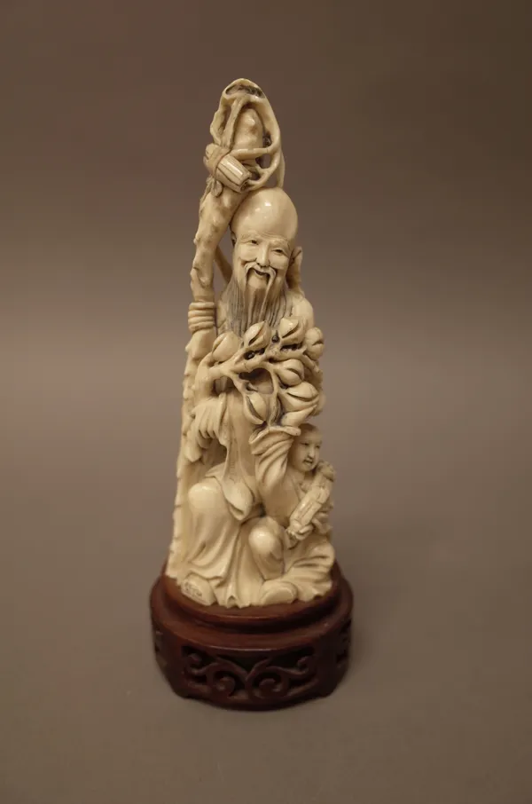 A Chinese ivory carving of Shoulao, early 20th century, carved standing holding a staff and branch of peaches, a child seated at his feet, 17cm. high,