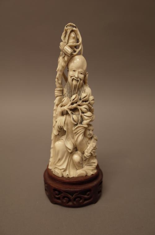 A Chinese ivory carving of Shoulao, early 20th century, carved standing holding a staff and branch of peaches, a child seated at his feet, 17cm. high,
