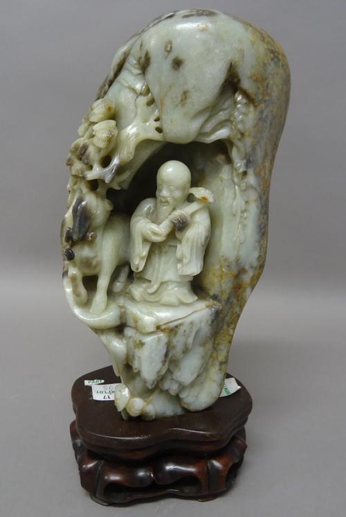 A Chinese mottled jade boulder carving, 18th/19th century, deeply carved to one side with Shoulao holding a ruyi sceptre standing beside a deer in a g